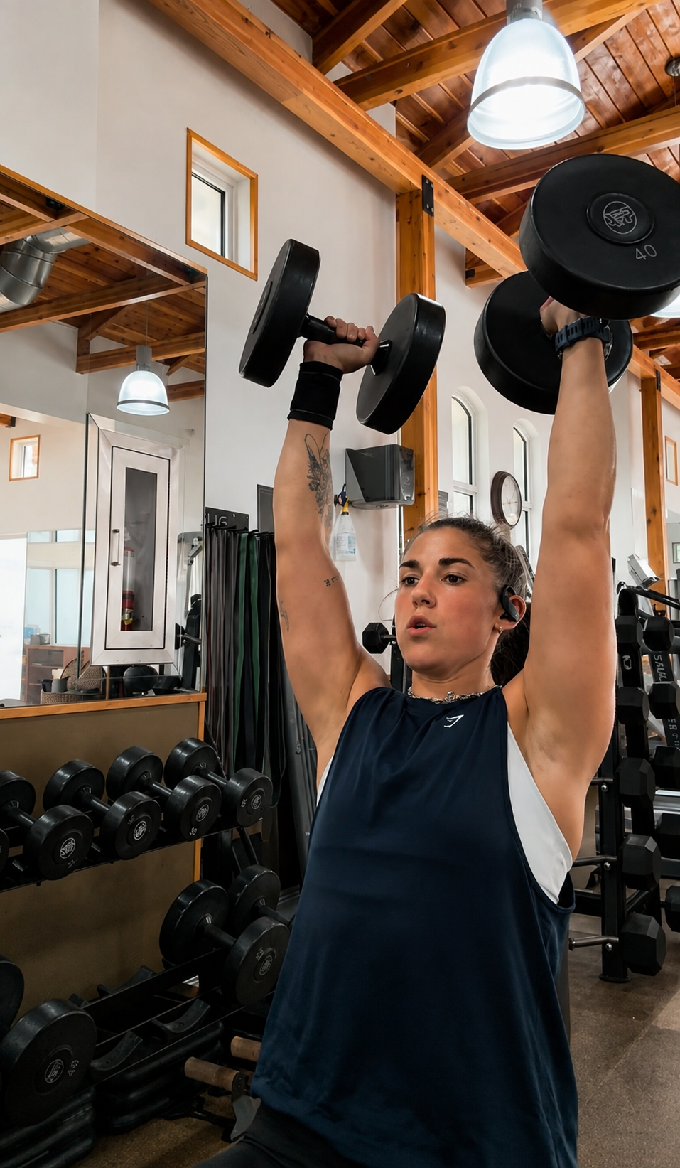 Athlete pressing dumbbells overhead in a strength training facility